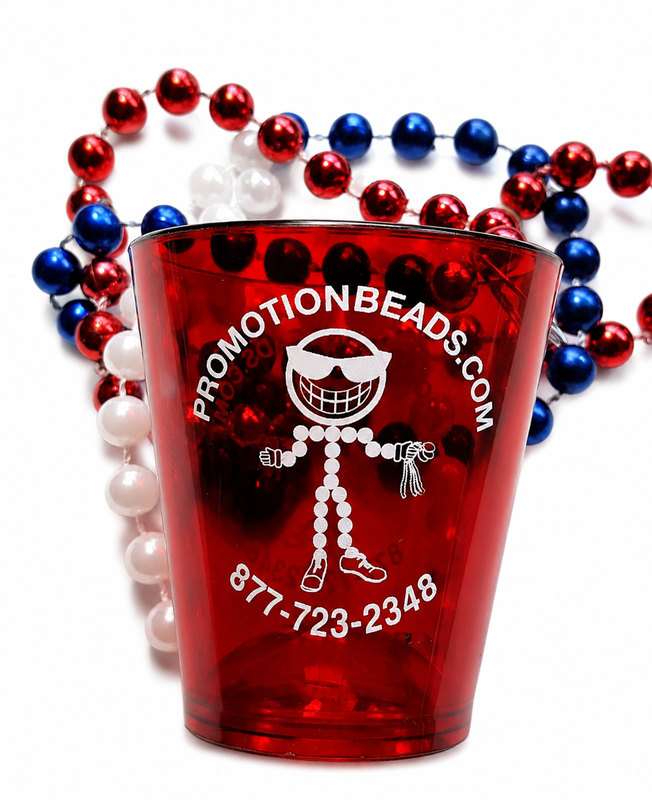 Red PromotionBeads.com shot glass with the Beadguy mascot print, on red, white and blue Mardi Gras beads